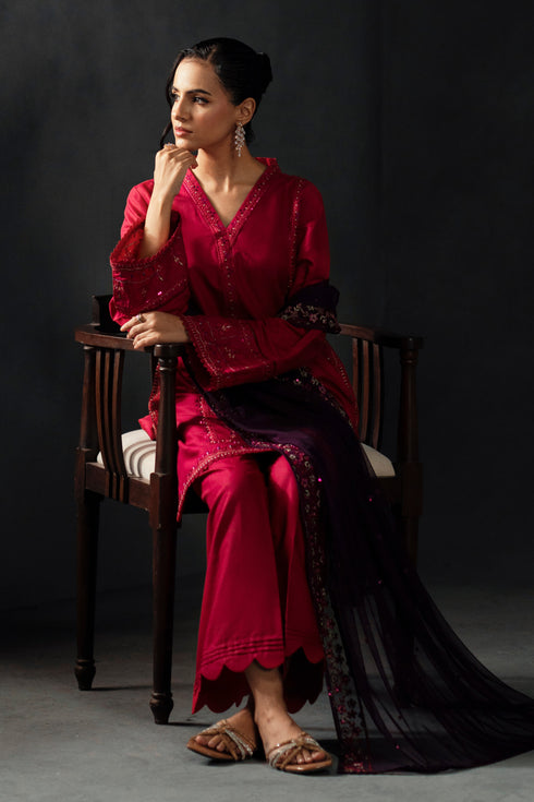 Woman in a red traditional outfit sitting on a wooden chair against a dark background